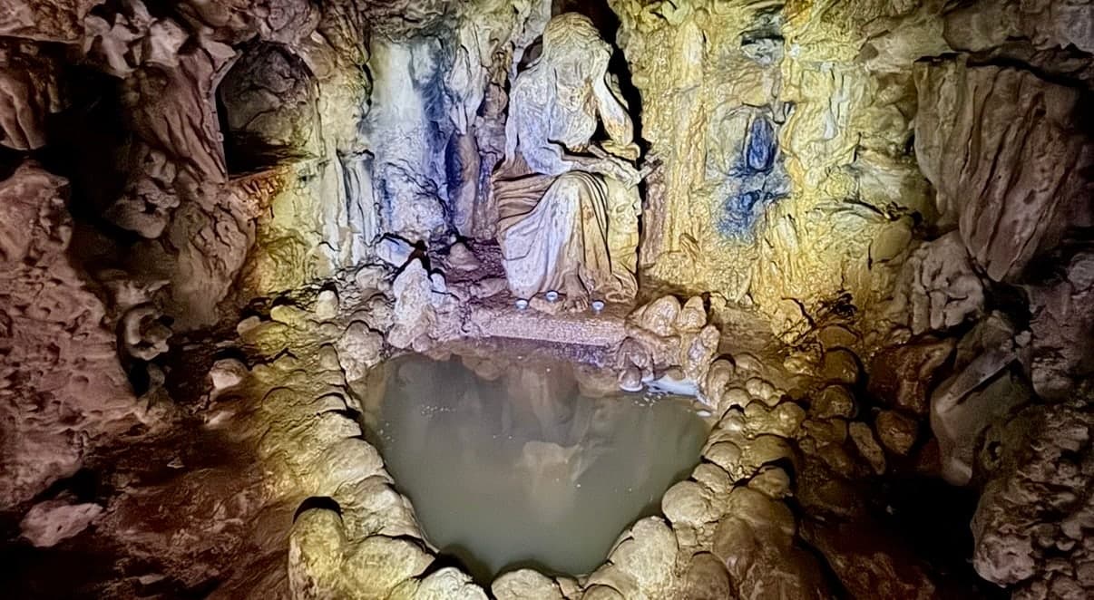 A candle-lit grotto with a statue of the Magdalene above a heart-shaped pool